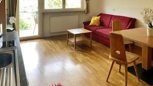 Uma sala de estar aconchegante com um sofá vermelho, mesa de centro de madeira e uma mesa de jantar com cadeiras.