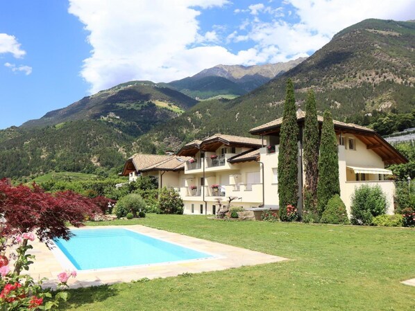 Un edificio de dos plantas con piscina, rodeado de exuberante vegetación y montañas al fondo.