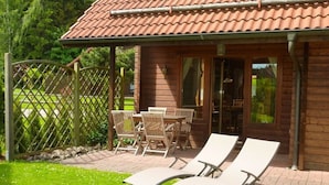 A wooden cabin with a tiled roof, a patio with a table and chairs, and two lounge chairs. - Doppelhaushalfte in Hasselfelde (Oberharz am Brocken)