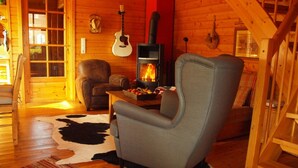 A cozy cabin interior with a fireplace, a leather armchair, a wooden floor, and a cowhide rug. - Doppelhaushalfte in Hasselfelde (Oberharz am Brocken)