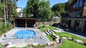 A backyard with a swimming pool, a covered patio, and a stone pathway. - Holiday Home With Pool and Sauna (Chmielno)