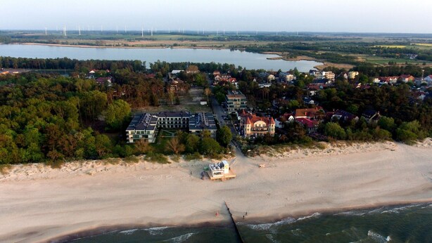 Oversigtsbillede af en kystby med strand, huse og vindmøller i det fjerne.