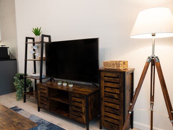 A wooden entertainment center with a flat-screen TV, a lamp on a tripod, and decorative items. - Apartment in Niechorze Near Baltic Beach (Rewal)