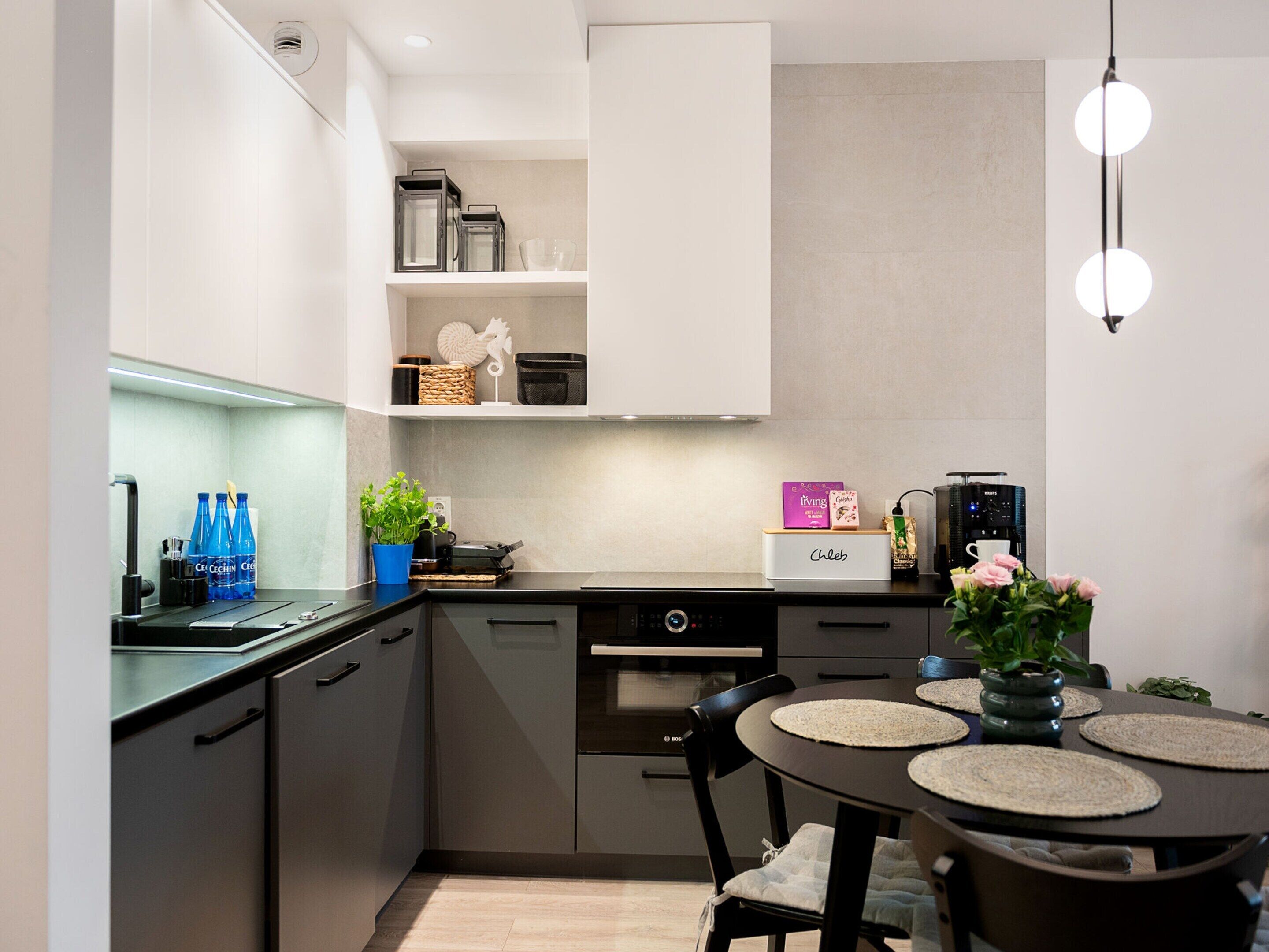 Una cocina moderna con horno empotrado, cafetera y comedor con mesa redonda y sillas.