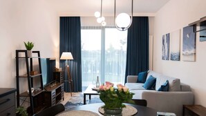 En moderne stue med sofa, spisebord og lampe. Gardiner ved vinduerne og kunst på væggene.