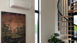 A modern interior with a wooden herringbone floor, a spiral staircase, a large artwork, and a green bench.