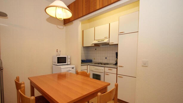 A compact kitchen with a wooden table and chairs, a microwave, a washing machine, and a stove. - Ferienwohnung im Haus Schiefertal, Wieda (Walkenried)