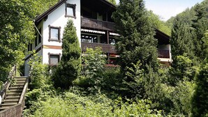 A two-story chalet with a balcony, surrounded by dense forest and a wooden staircase leading to the entrance. - Ferienwohnung im Haus Schiefertal, Wieda (Walkenried)