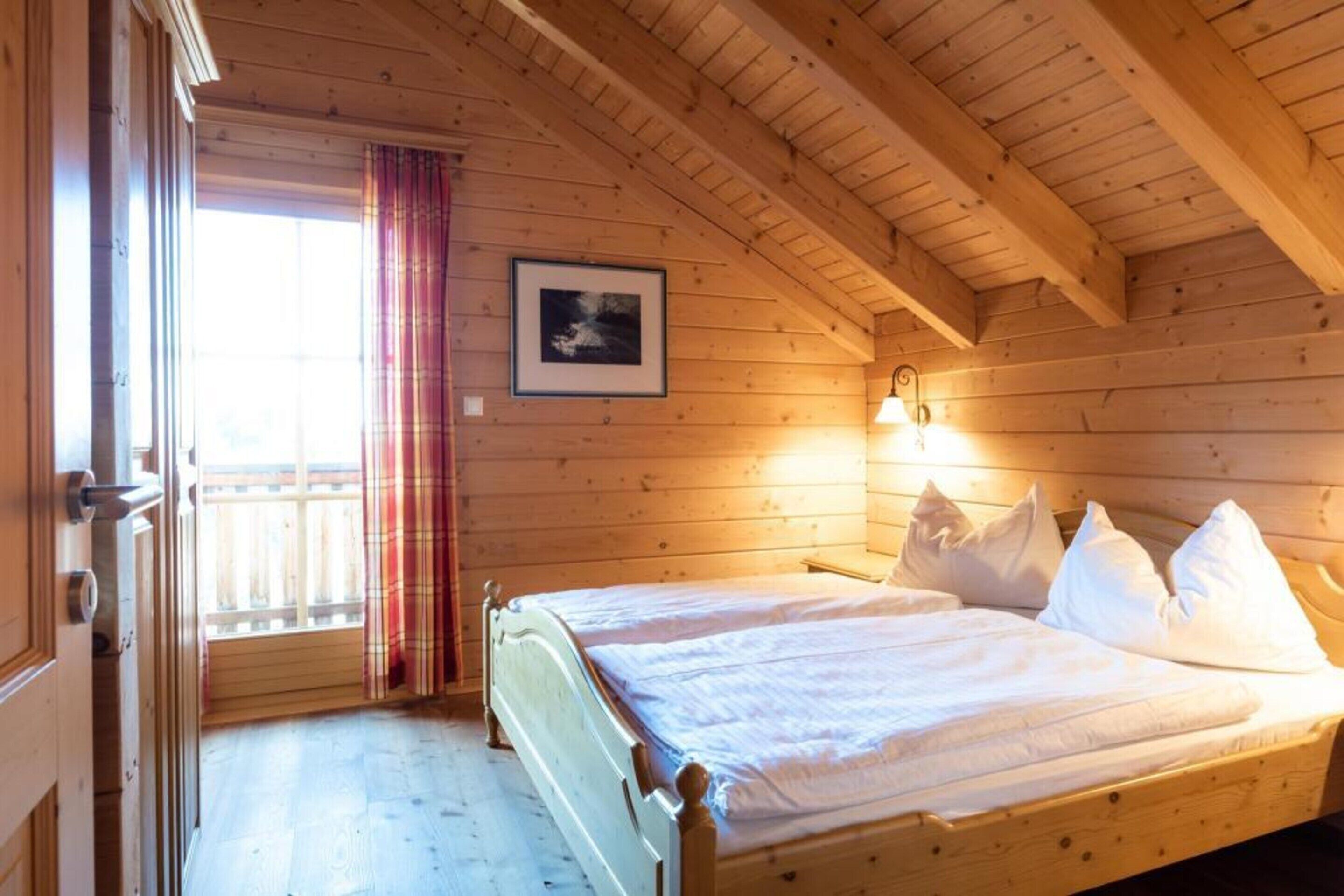 A wooden cabin bedroom with a bed, a window with curtains, and a framed picture on the wall.