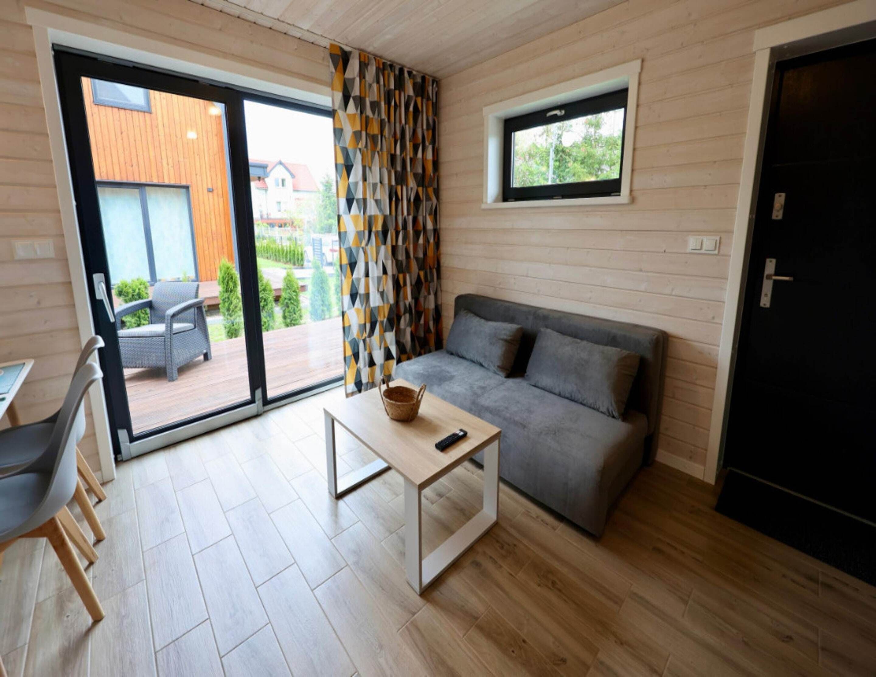 A modern living room with a grey sofa, a small table with a basket, and a sliding glass door leading to an outdoor area.