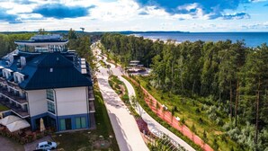 A modern building with a rooftop terrace, a paved pathway, and a forested area with a view of the sea. - Condo in Swinoujscie Near Baltic Sea Beach (Swinoujscie)