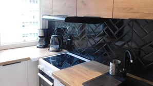 A modern kitchen with wooden cabinets, a black backsplash, a stove, and a coffee maker. - Condo in Swinoujscie Near Baltic Sea Beach (Swinoujscie)