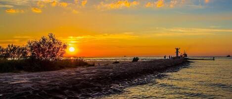 A sunset over a rocky shoreline with a pier extending into the water.