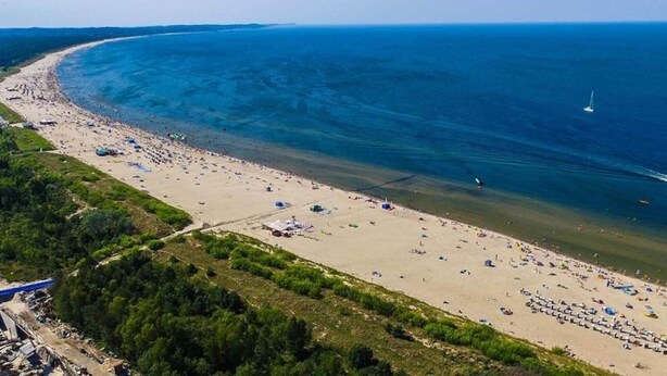 An aerial view of a beach with a curved shoreline, a jet ski, and a sailboat. - Condo in Swinoujscie Near Baltic Sea Beach (Swinoujscie)