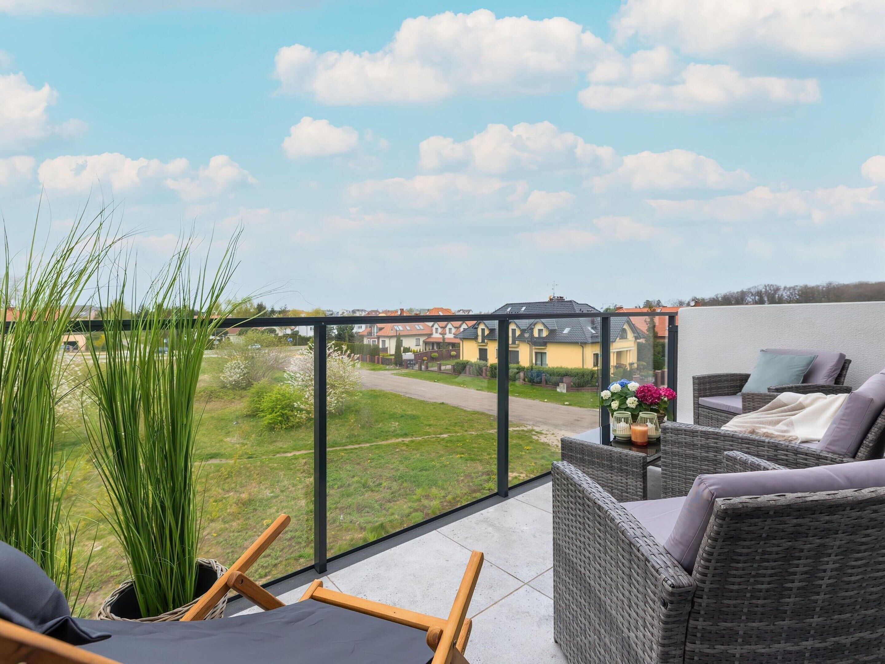 A balcony with wicker furniture, a view of houses, and a grassy area.