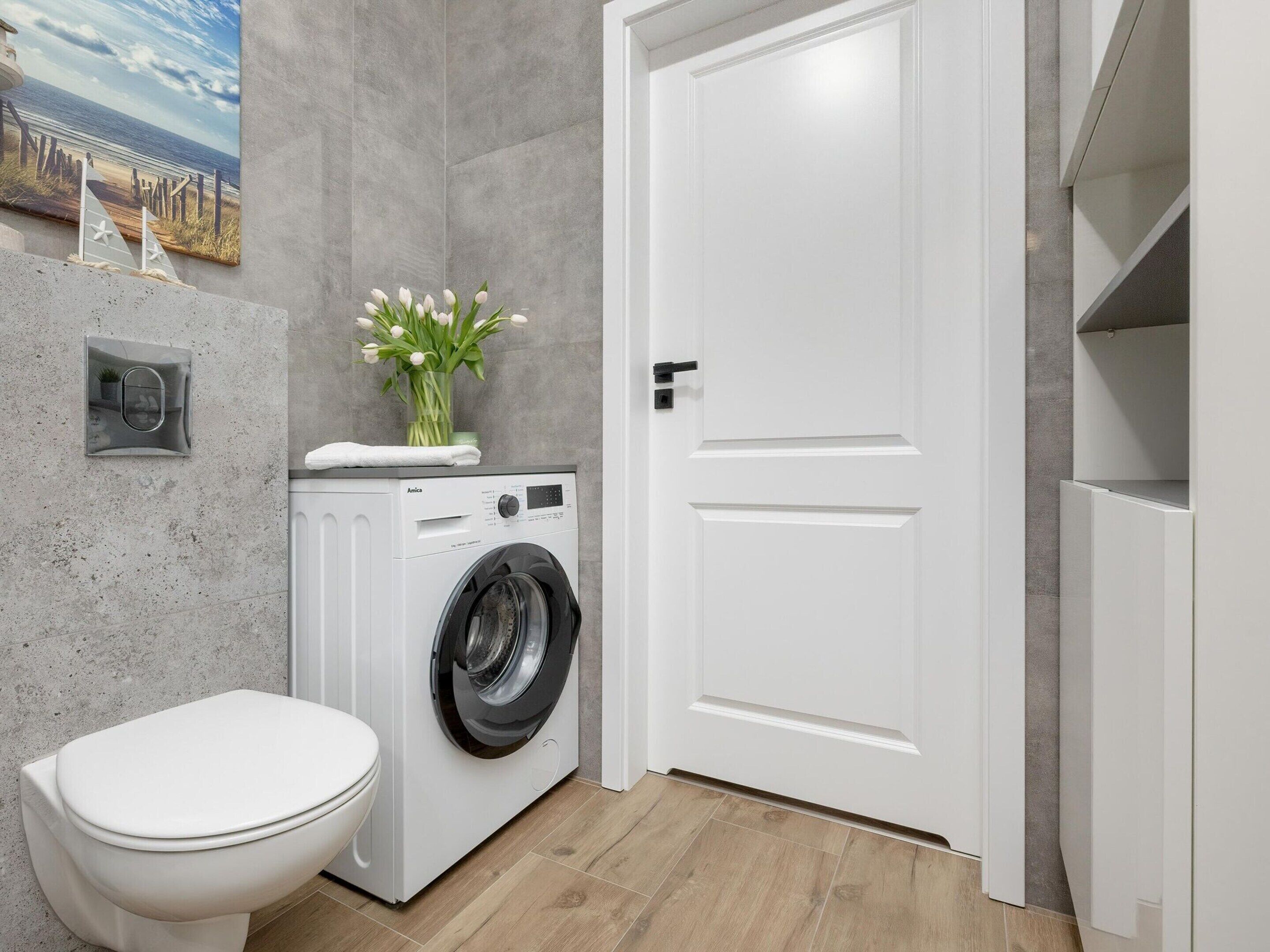 A compact laundry room with a washing machine, a toilet, and a door.