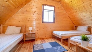 A cozy wooden cabin with two single beds, a small table, a nightstand, a window, and a potted plant. - Comfortable Holiday Home in Jaroslawiec (Postomino)