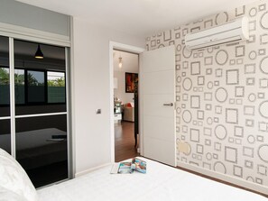 Un dormitori amb una porta corredissa que dona a una cuina, paper tapet i una revista a terra.