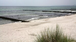 Una spiaggia con un litorale sabbioso e onde che si infrangono sulla riva. Sono presenti barriere frangiflutti in legno che si estendono nell'acqua per prevenire l'erosione.