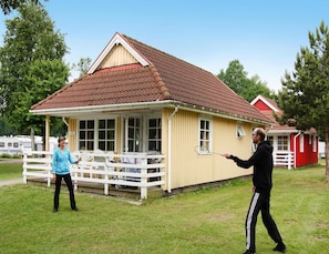 A small yellow building with a red roof, a white porch, and a red structure in the background.