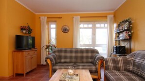 Una sala de estar con un sofá tapizado en cuadros, una mesa de centro de madera, un televisor sobre un mueble de madera y una ventana con cortinas.