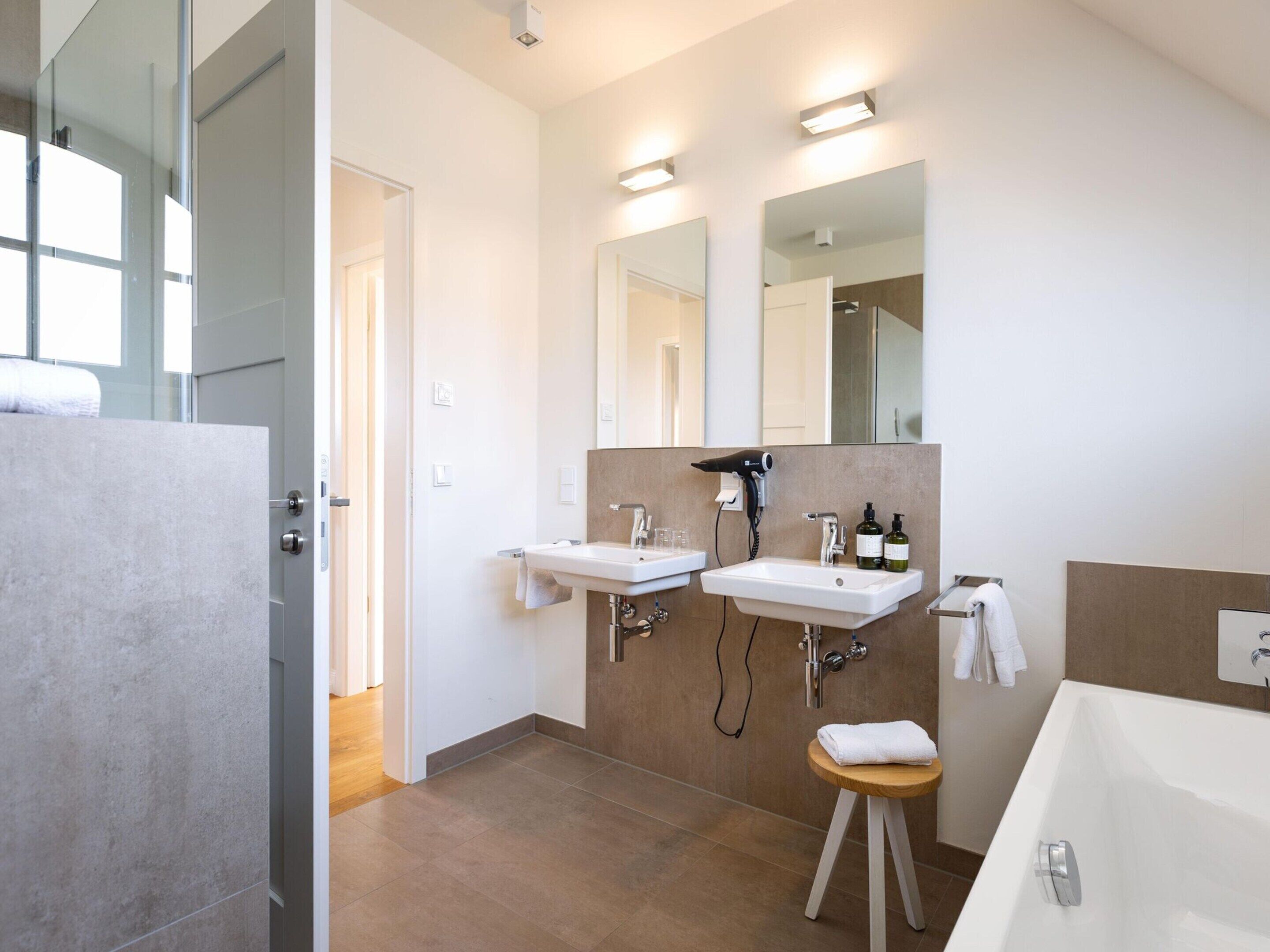 A modern bathroom with two sinks, a hairdryer, and a bathtub.