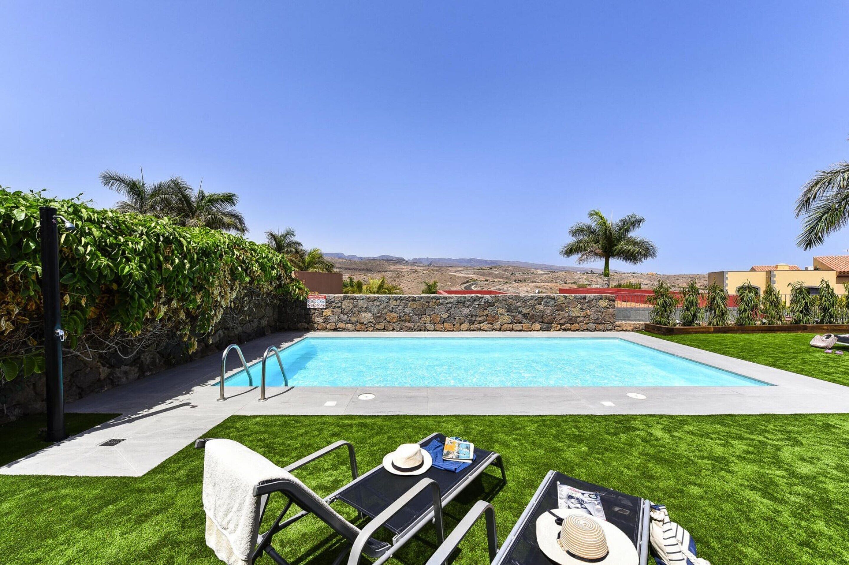 A swimming pool with a stone wall, surrounded by a well-maintained lawn and palm trees.