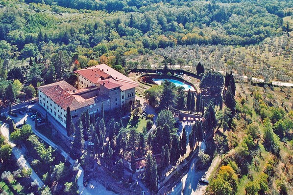 An aerial view of a large building with a swimming pool surrounded by trees.