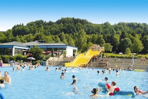 En offentlig swimmingpool med et gult vandrutsjeban og en skovklædt bakke i baggrunden.