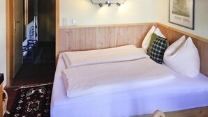 Une chambre d’hôtel avec une tête de lit en bois, un lit recouvert de draps blancs, un luminaire fixé au mur et un tableau encadré accroché au mur.