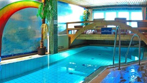 Une piscine intérieure aux carreaux bleu clair, dotée d’une plage en bois et d’un panneau indiquant la profondeur de la piscine.