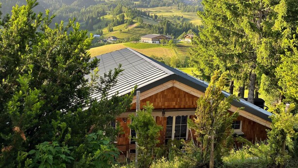 Une cabane en bois, dotée d’un toit en pente, entourée d’une végétation luxuriante et avec des montagnes en toile de fond.