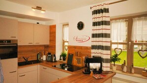 A kitchen with wooden cabinets, a coffee machine, and a window with heart-shaped decorations. - Ferienwohnung in Bodenmais am Grossen Arber (Bodenmais)