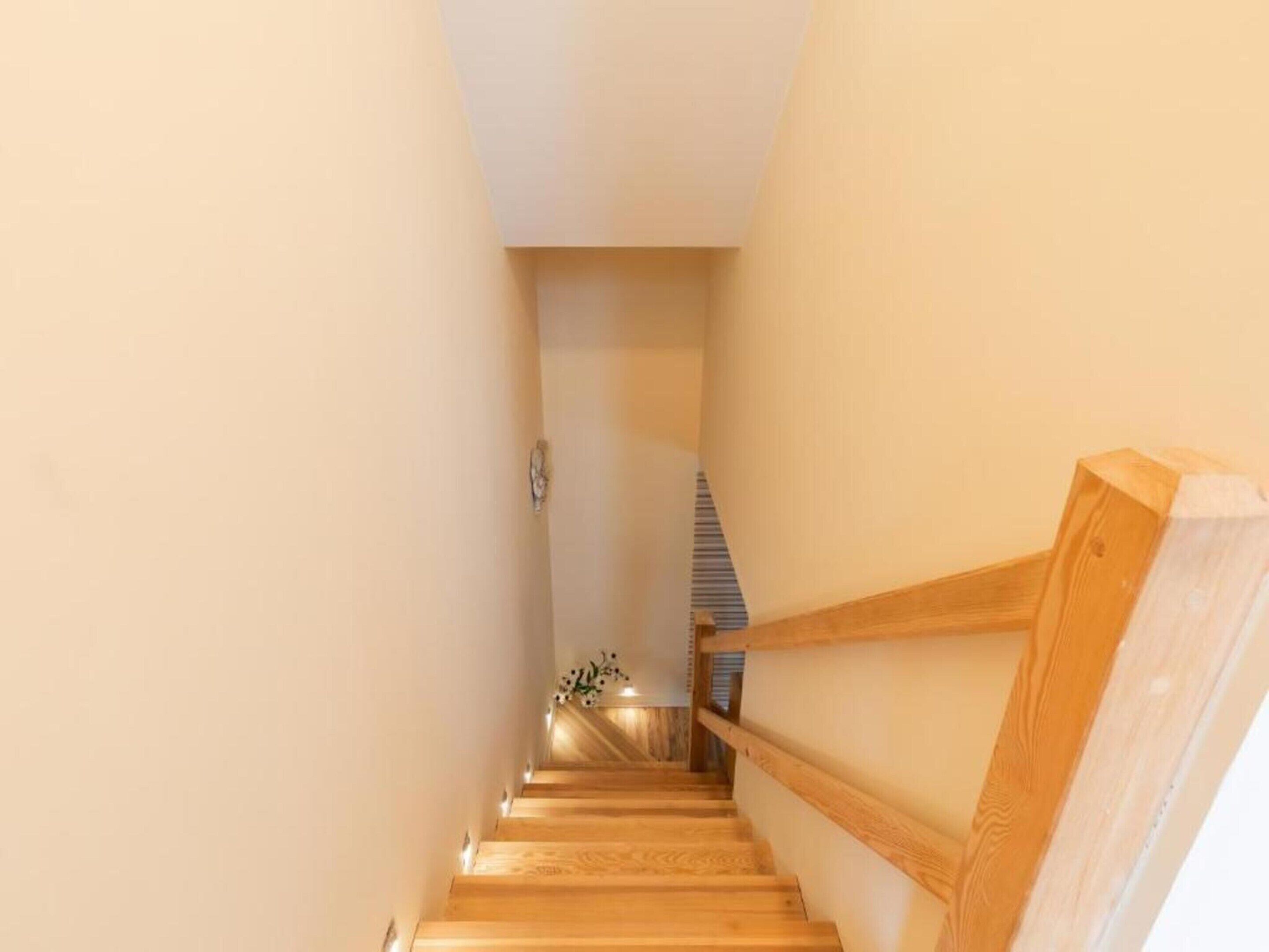 A wooden staircase with a handrail, leading to a room with a striped ceiling.
