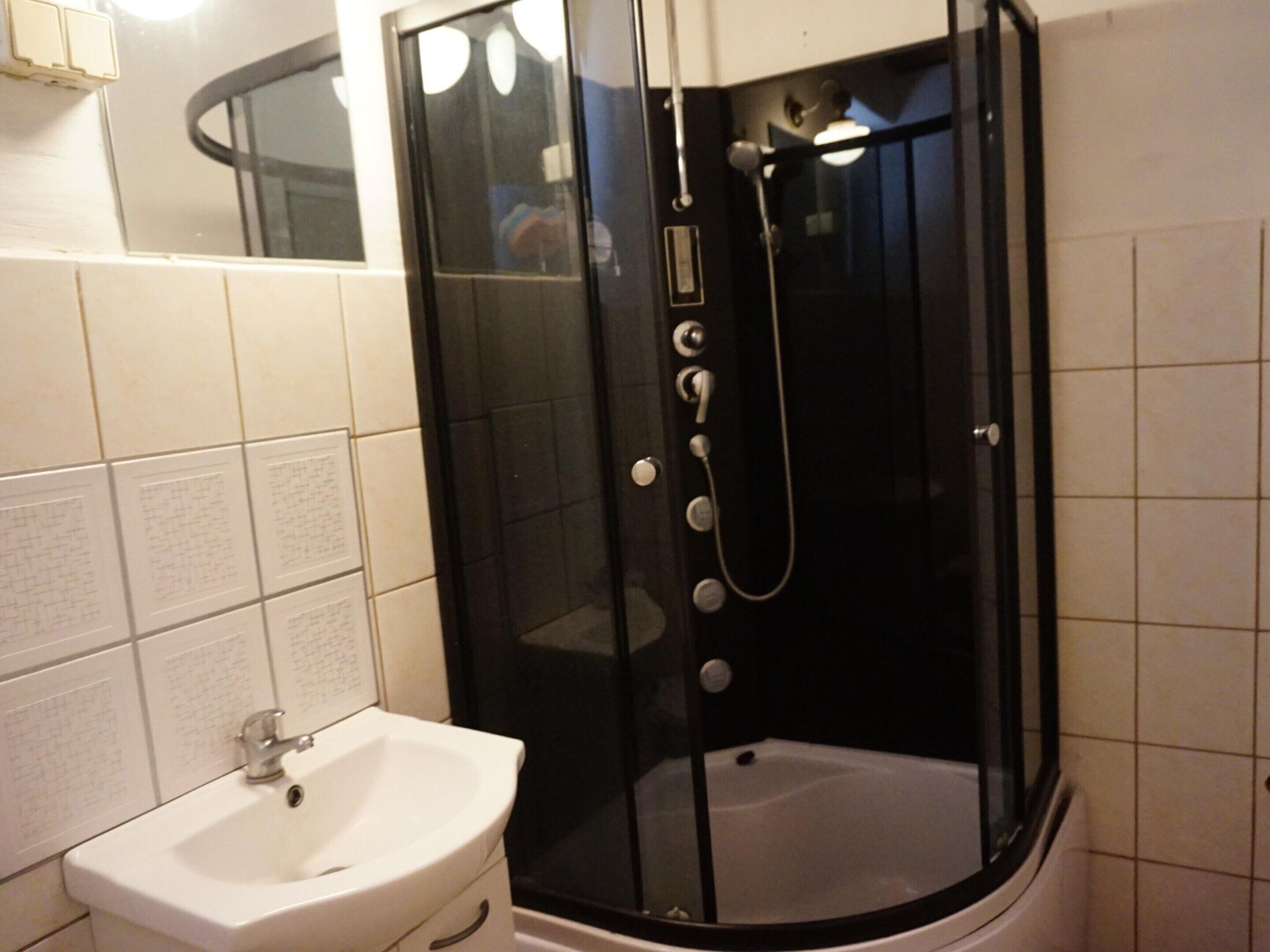 Une salle de bain avec un lavabo blanc, une douche à parois de verre et des murs recouverts de carreaux blancs.