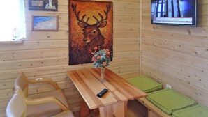 A wooden cabin interior with a dining table, chairs, a TV, and a deer rug.