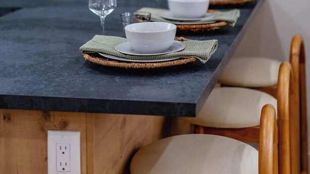Une cuisine moderne avec un plan de travail foncé, des chaises en bois et un pare-feu orné d’un motif géométrique.