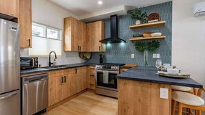 Une cuisine moderne avec des meubles en bois, des appareils en acier inoxydable, une hotte noire et un pare-feu en carreaux.