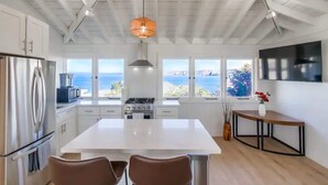 A modern kitchen with a large island, white cabinetry, stainless steel appliances, and a view of the sea. - Spectacular La Jolla Cove Compound (San Diego)