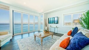 A spacious living room with a large window overlooking the sea, a wooden coffee table, a sofa with colorful cushions, and a flat-screen TV mounted on the wall. - Spectacular La Jolla Cove Compound (San Diego)