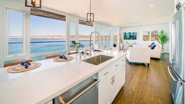 A modern kitchen with a large island, a view of the sea, and a dining area with a white sofa. - Spectacular La Jolla Cove Compound (San Diego)