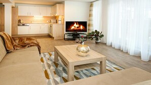 Un salon moderne avec un canapé, une table basse agrémentée d’objets décoratifs, un téléviseur diffusant une image de feu, et une cuisine en arrière-plan.