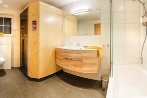 Ein modernes Badezimmer mit einem Holzkosmetikschrank, einer Glasdusche und einer weißen Badewanne.