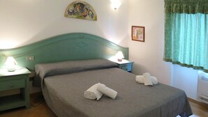 A bedroom with a green bed, two bedside tables with lamps, a painting on the wall, and a window with a green curtain. - Villa on Costa Rei Near Sandy Beach (Muravera)