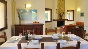 A dining area with a table set for two, a television, and a stone fireplace. - Villa on Costa Rei Near Sandy Beach (Muravera)