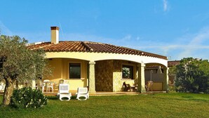 A house with a tiled roof, a covered patio, and a lawn with outdoor furniture. - Villa on Costa Rei Near Sandy Beach (Muravera)