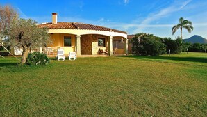 A house with a tiled roof, a covered patio, and a well-maintained lawn. - Villa on Costa Rei Near Sandy Beach (Muravera)