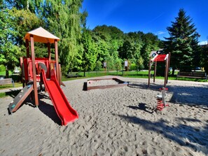 A playground with a red slide and climbing structures, surrounded by sand and trees. - Holiday Home in Ustronie Morskie Near Beach (Ustronie Morskie)