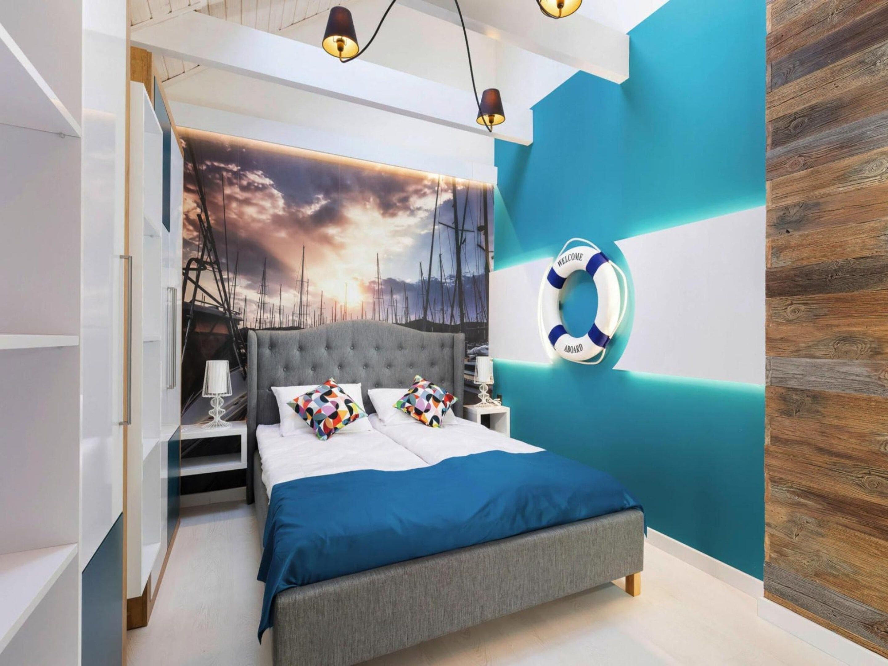 Une chambre moderne avec un grand lit, un dispositif de sauvetage fixé au mur et une fresque représentant un coucher de soleil.