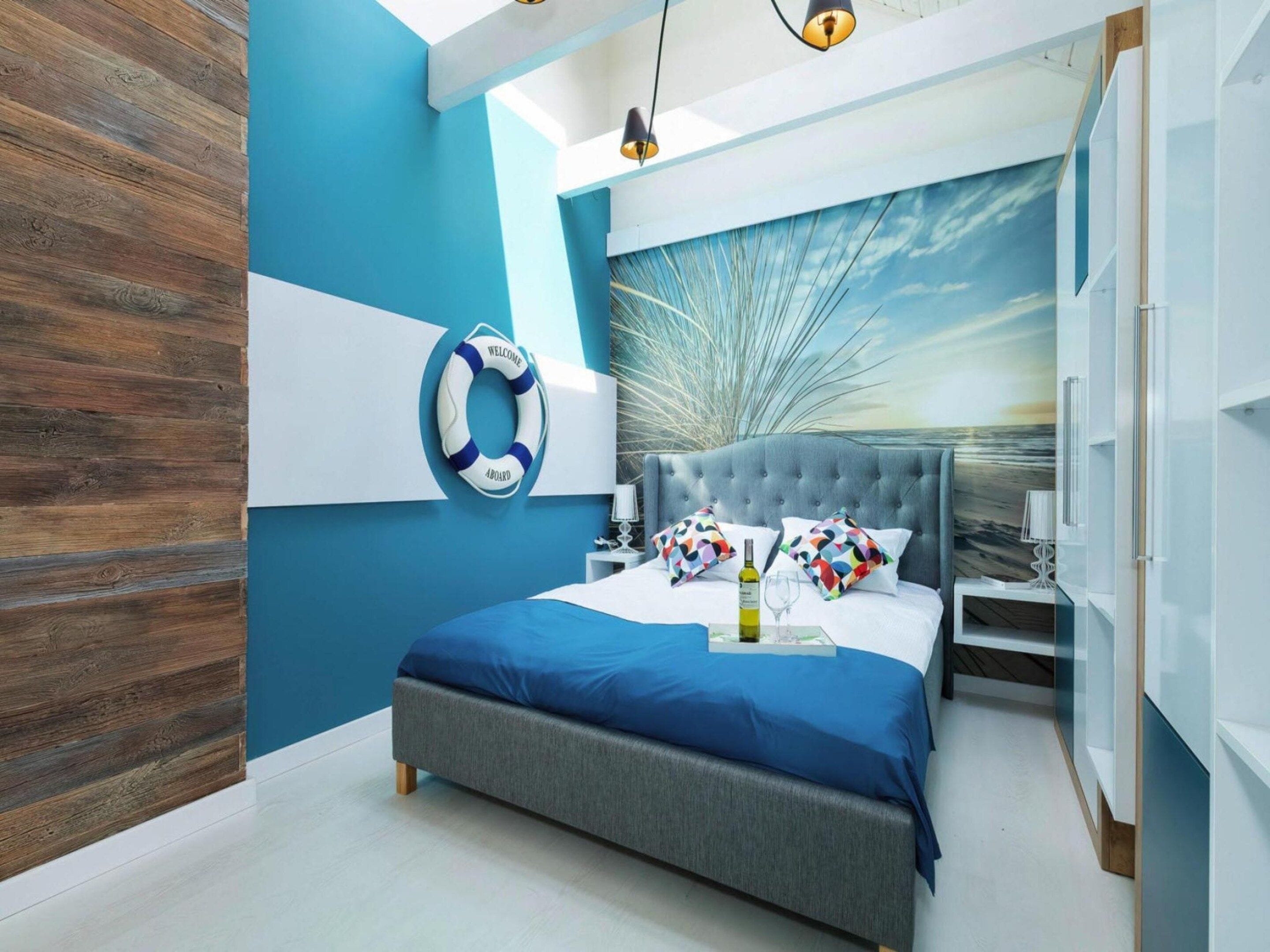 Ein modernes Schlafzimmer mit einem großen Bett, einer an der Wand befestigten Rettungsboje und einem Wandgemälde mit Meereslandschaft.